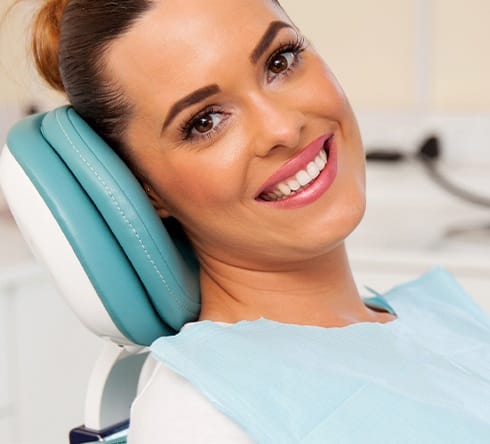 Woman smiling in dental chair after teeth whitening
