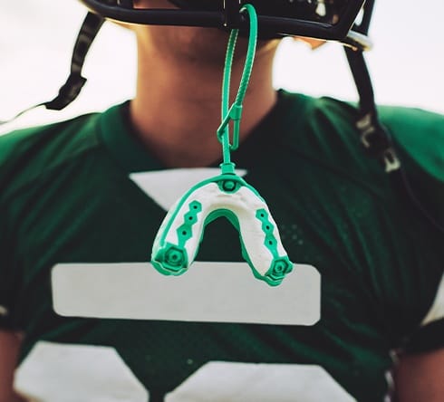 Football player with athletic mouthguard hanging from mask