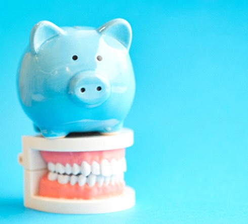 Piggy bank atop model teeth representing cost of cosmetic dentistry in Fort Valley
