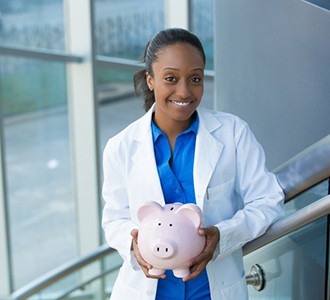 smiling dentist holding a pink piggy bank