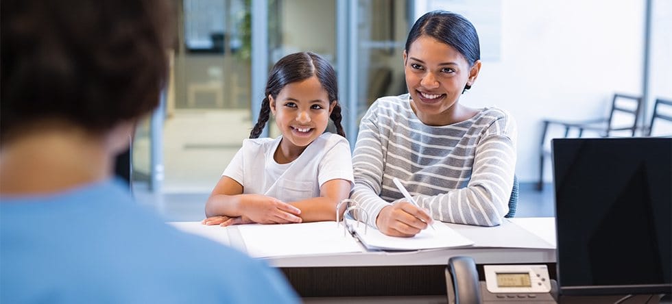 Mother and daughter filling out dental insurance forms at front desk