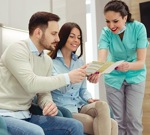 Dental team member giving man and woman dental insurance forms