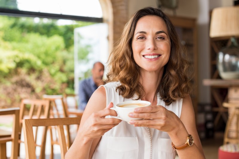 Woman with dental implants smiling while drinking coffee