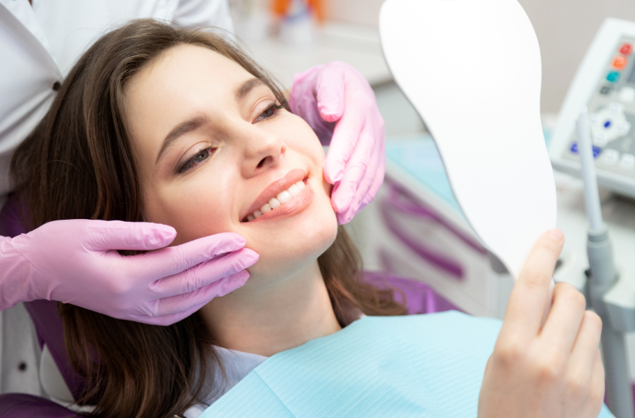 Woman in dentist's chair looking at hand mirror, smiling